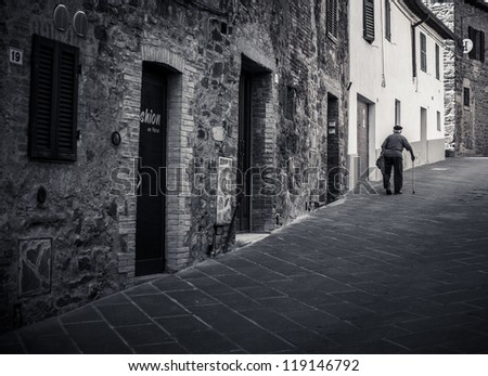 Old man walking in a medieval street in Tuscany, Italy