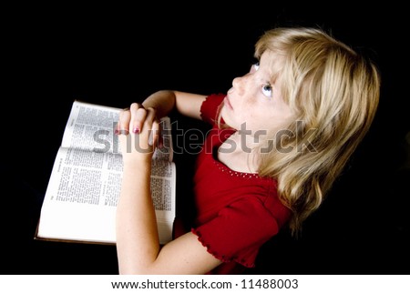 Angelic little girl saying her prayers over an open New Testament.