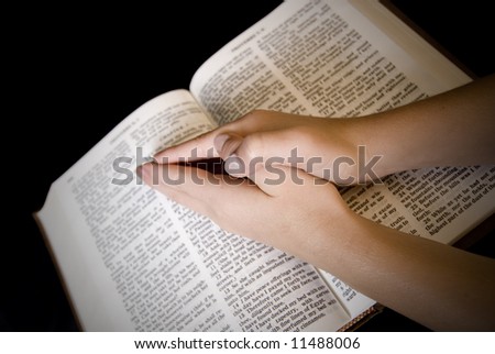 Child\'s hands clasped in prayer atop New Testament