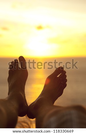 Male feet in relaxed pose silhouetted by sunset over ocean