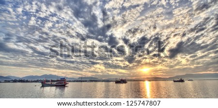 Sunrise over lake in south of thailand with finish boats in foreground and mountains in the distance