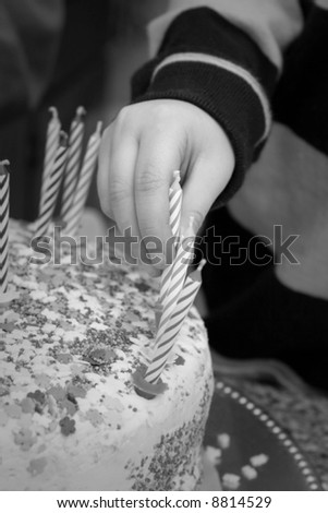 child\'s hand places candle on cake - black and white