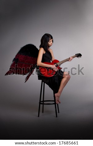 young woman in black dress & black angel wings plays guitar