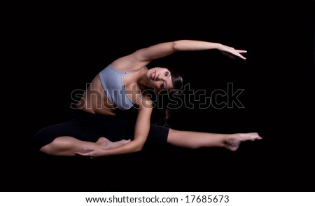 long & lean dancer in seated stretch looking at camera - black background
