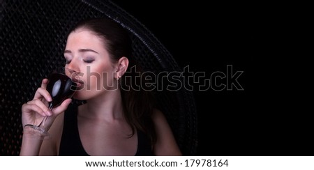 beautiful woman relaxes drinking wine - black background & room for copy