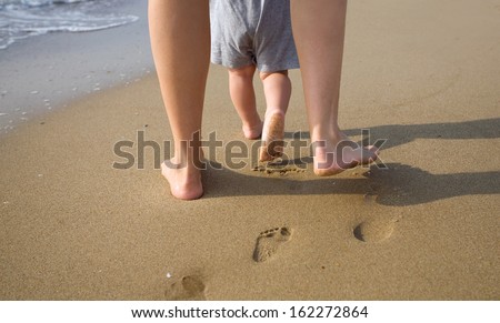 mom helps to make the child\'s first steps on the beach