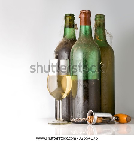three old bottles of wine, a glass and a corkscrew on a light background