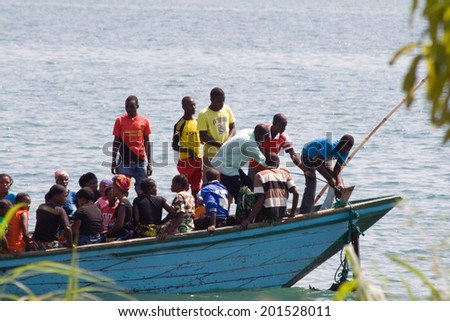 MPULUNGU, ZAMBIA - JUNE 6, 2014: Unidentified people sit in a boat, one unidentified man lifts the anchor before departure at the beach in Mpulungu on June 6, in Zambia 2014.