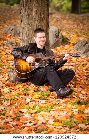 Teenage boy playing the guitar in a pile of fall leaves