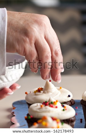Chef decorating and piping buttercream icing on chocolate filled chocolate cupcakes - baker putting sprinkles on