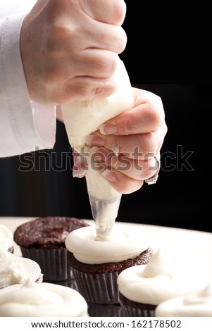 Chef decorating and piping buttercream icing on chocolate filled chocolate cupcakes