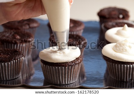 Chef decorating and piping buttercream icing on chocolate filled chocolate cupcakes - hand