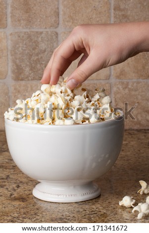 Hand grabbing freshly popped popcorn in a vintage ceramic bowl on granite counter
