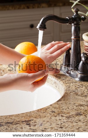 Freshly harvested California Oranges with running water at a sink; hands turning off faucet