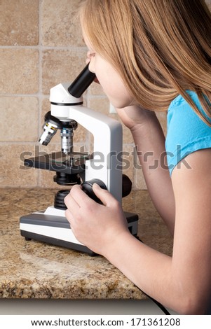 Young Caucasian girl with blonde hair examining a specimen through a microscope