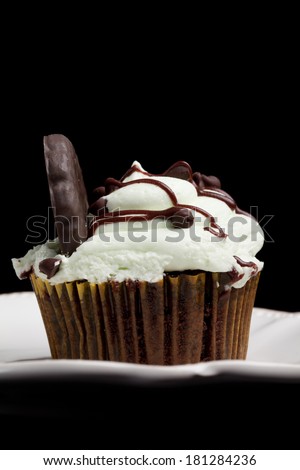 Delicious chocolate mint cupcake with miniature chocolate chips sprinkled on top with drizzled melted chocolate and a chocolate mint cookie on a black background