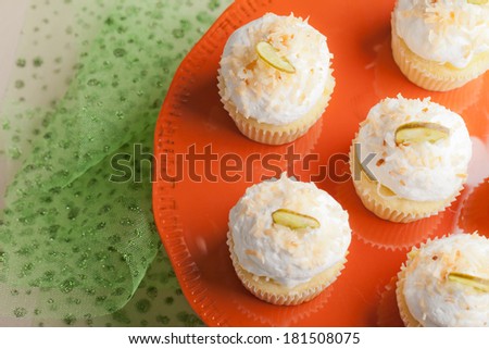 Top view of Coconut Key Lime Cupcakes on a retro orange platter (vintage) - Coconut cake with a key lime filling topped with a light 7 minute frosting, toasted coconut, and a slice of candied key lime