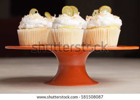 Coconut Key Lime Cupcake s on a vintage orange platter black background - Coconut cake with a key lime filling topped with a light 7 minute frosting, toasted coconut, and a slice of candied key lime
