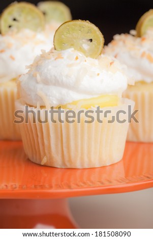 Macro shot of Coconut Key Lime Cupcakes on a retro vintage orange platter - Coconut cake with a key lime filling topped with a light 7 minute frosting, toasted coconut, and a slice of candied key lime