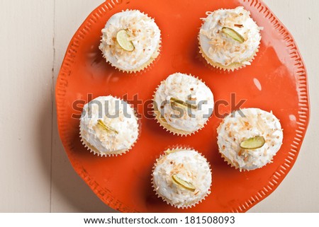 Coconut Key Lime Cupcakes on a vintage retro orange cake platter top view - Coconut cake with a key lime filling topped with a light 7 minute frosting, toasted coconut, and a slice of candied key lime