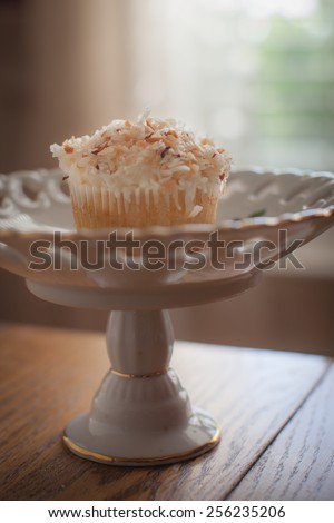 Macro shot of White chocolate cream cupcake with toasted coconut on top on a tall vintage platter