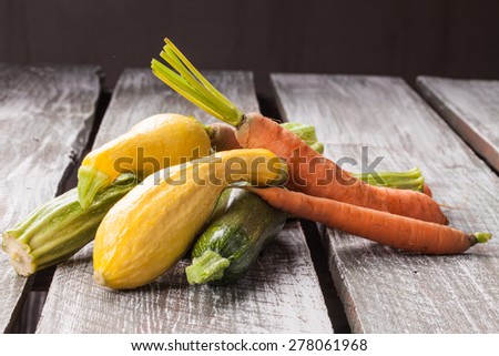 Macro shot of freshly harvested carrots, yellow summer squash, and Romanesco Italian zucchini on an old barn wood table side view not cropped