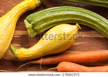 Macro shot of freshly harvested carrots, yellow summer squash, and Romanesco Italian zucchini on a bamboo cutting board