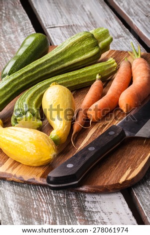 Macro shot of freshly harvested carrots, yellow summer squash, and Romanesco Italian zucchini on an old barn wood table, cutting board, with a chef\'s knife