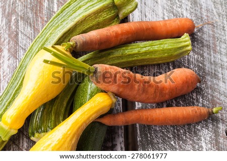 side view of a macro shot of freshly harvested carrots, yellow summer squash, and Romanesco Italian zucchini on an old barn wood table