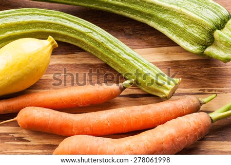Macro shot of freshly harvested carrots, yellow summer squash, and Romanesco Italian zucchini from top on a bamboo cutting board