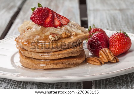 Plate of a stack of organic whole wheat pumpkin pancakes topped with apple cinnamon spiced syrup, strawberries, and pecans