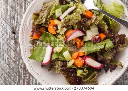 Top view of a vintage plate with an Italian chopped green garden salad on an old barn wood table