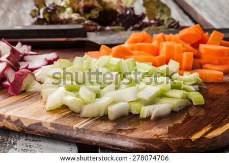 macro shot side view of a bamboo cutting board with chef\'s knife with freshly chopped organic carrots, lettuce, celery, and radishes