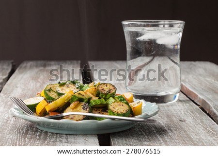 Side shot of a plate of freshly sauteed summer vegetables on an old barn wood table with a clear glass of water