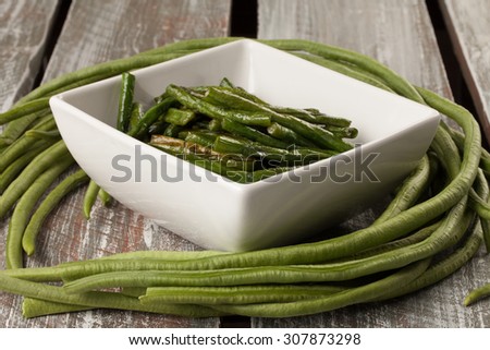 Freshly harvested Asian green beans on a weathered barn wood table with a white bowl of stir-fried beans