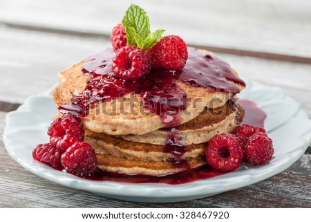 Whole wheat oatmeal pancakes with boysenberry sauce topped with red raspberries and a mint sprig macro shot on a weathered barn wood table