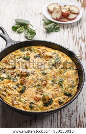 Baked egg frittata with spinach, cheese, broccoli, red potatoes, bacon, milk, and spinach close up on weathered white wood