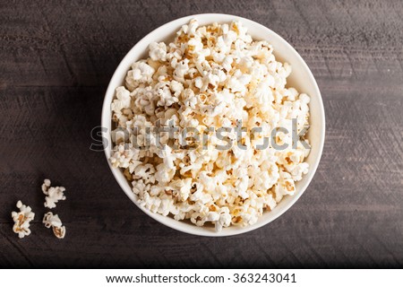 Olive oil popped popcorn in a porcelain bowl top view on a dark wooden background