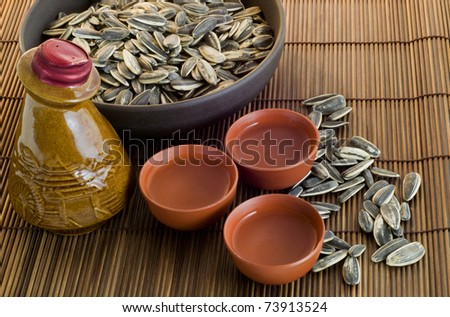 Chinese antique wine bottle with wine cups and sunflower seeds on brown bamboo table mat.