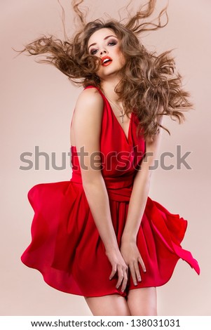 Young woman in short red dress, beautiful hairstyle and make up - posing in studio