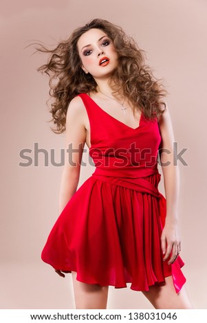 Young woman in short red dress, beautiful hairstyle and make up - posing in studio