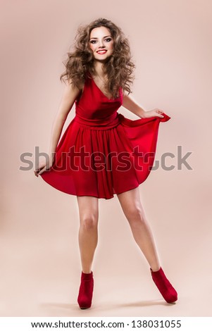Young woman in short red dress, beautiful hairstyle and make up, she is smiling - posing in studio
