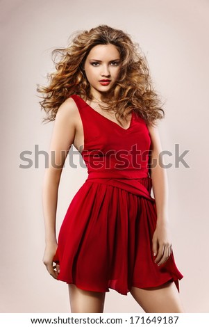 Beautiful girl with long curly hair in red dress, work in studio