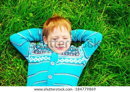 Little happy boy laying in the green grass, outside