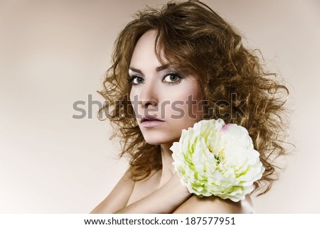 Beautiful woman with curly hairstyle, makeup, closeup, flower in her blonde hair, work in studio