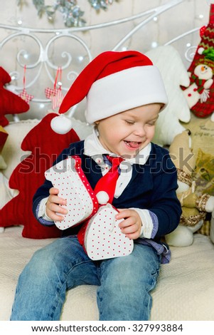 Cheerful little boy playing with gifts, he in the red hat of Santa