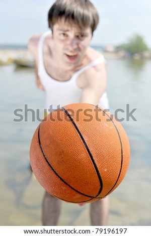 Handsome guy standing on the rocky beach in water holding a basketball ball