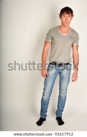 Fashion full-length portrait of the young beautiful man in white t-shirt posing over gray background, series photo