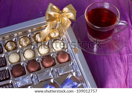 Holiday box of chocolates next cup of tea on a violet background