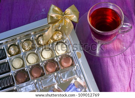 A cup of tea next to a box of sweets on a violet background
